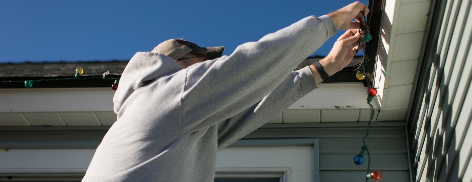 man hanging holiday lights on gutter of house